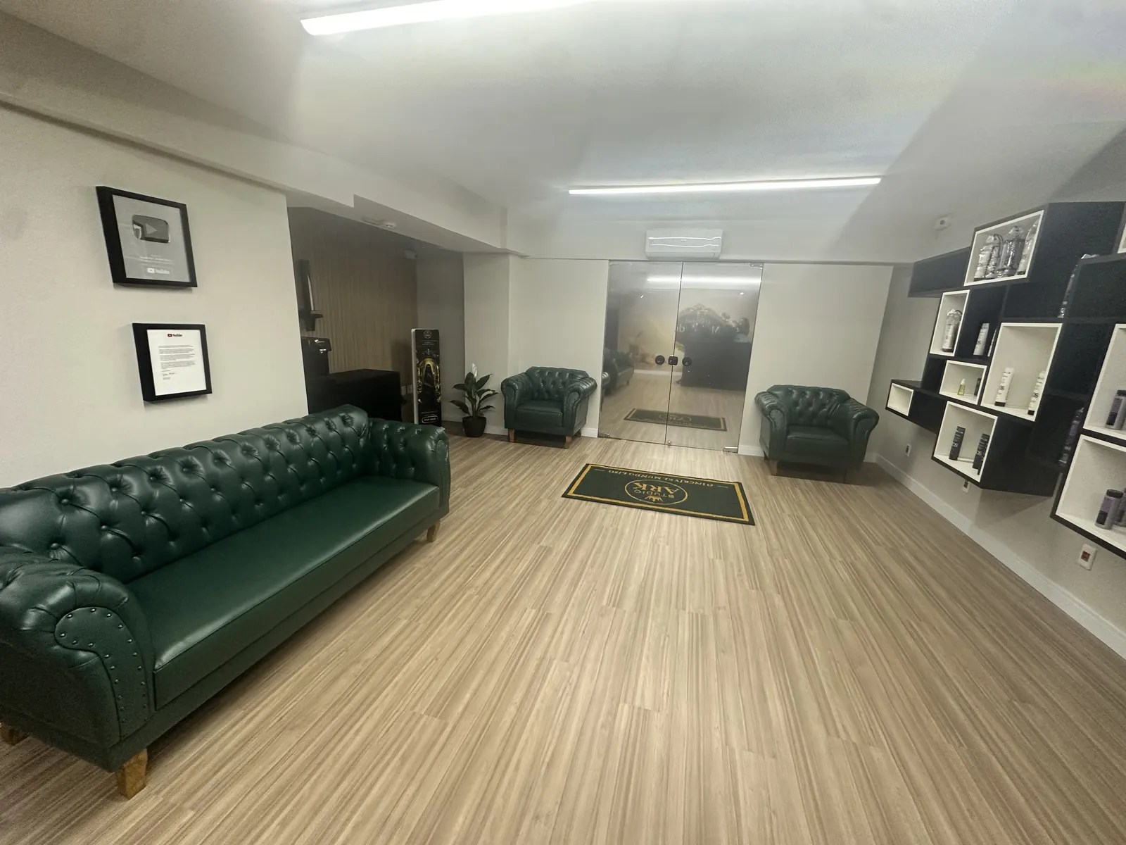 Recepção do Studio Ark com sofá e poltronas verdes, piso de madeira e exposição de produtos.